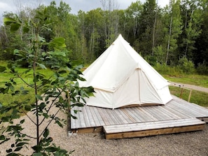 Een witte tent met een houten terras in een bebost gebied.