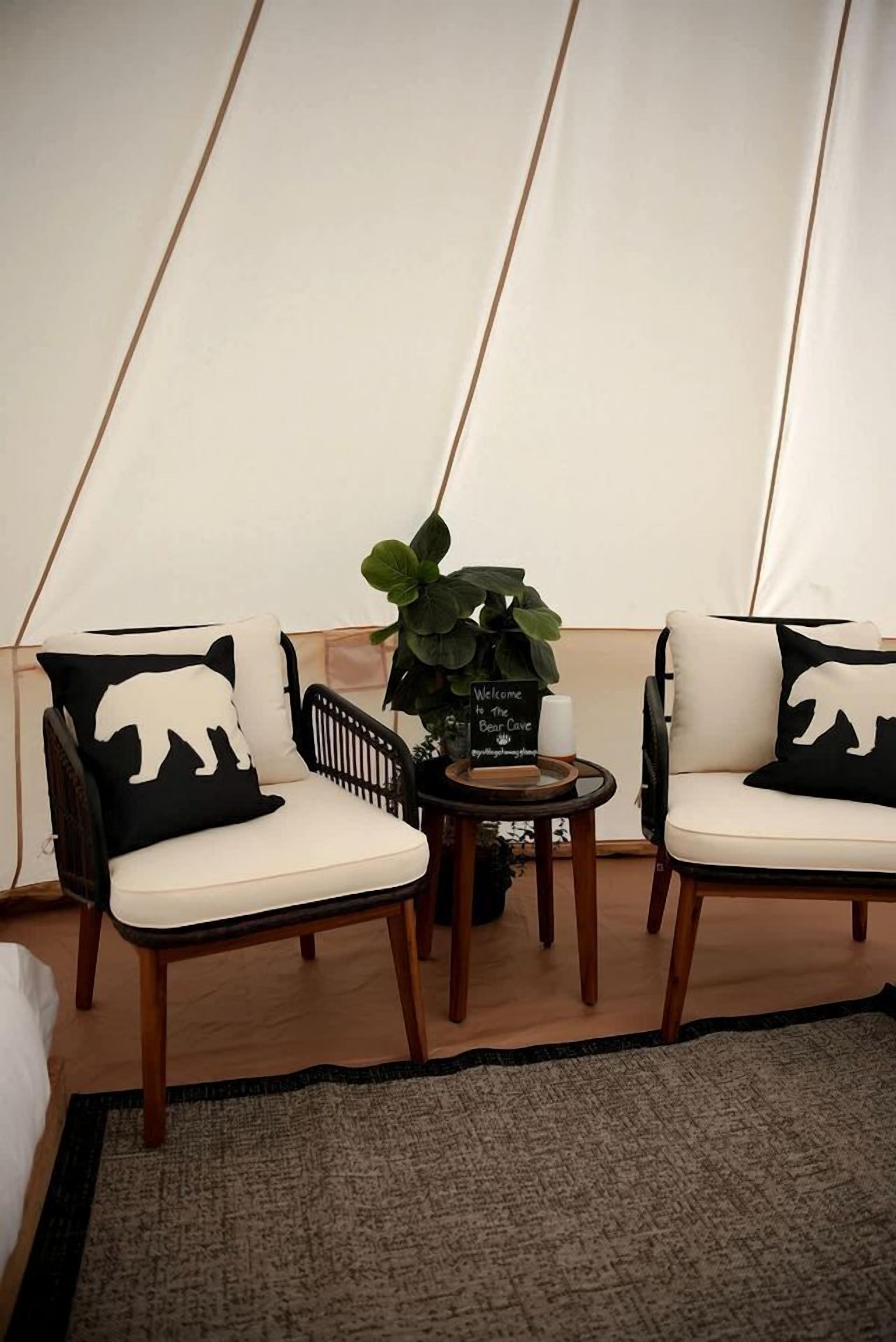 A tented room with two chairs, a small table with a candle, a welcome sign, and a potted plant.