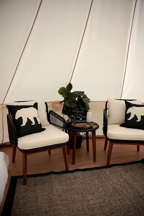 Een tent met twee stoelen, een kleine tafel met een kaars, een welkomstbord en een potplant.