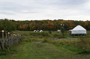 A rural landscape with a white tent, a windmill, and a fenced area with spherical posts. - Yurt with Pond Access for Glamping Escapes in Ontario, Canada (Powassan)
