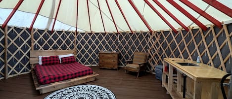 Een tent met een bed, een stoel, een tafel en een tapijtend.