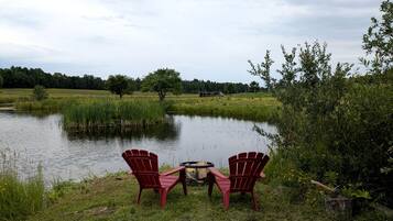 Twee Adirondack-stoelen gericht op een vijver met een vuurkuil in het midden.