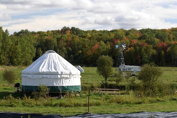 A yurt with a windmill in a grassy field.