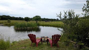 Two Adirondack chairs facing a pond with a fire pit in the center.