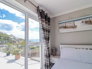 A bedroom with a bed, a nightstand, a lamp, a window with curtains, and a painting on the wall.