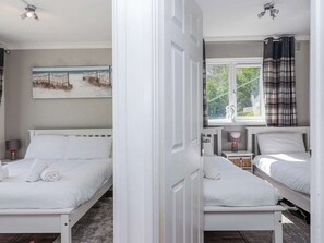 A bedroom with two beds, a window with curtains, a bedside lamp, and a painting on the wall.