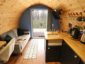 A cozy cabin interior with a sofa, a small kitchen area, and a view through a window. - Hobhole, in Keal Cotes, 1-bed. (Spilsby)