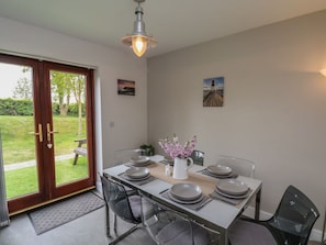 A dining area with a table set for four, a white vase with flowers, and a view through a glass door to a garden. - Buffers: Cozy Retreat in Whitby (Whitby)