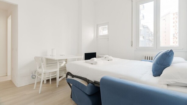 A hotel room with a bed, a desk, and a chair. - GuestHost - Comfortable 30m2 studio flat, perfect for 2 people, located on the mezzanine floor of a building (steps to access).The accommodation is located in the Calvairate district, a residential area characterized by the green heart of Piazza Insubria (Milan)