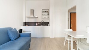 A modern living space with a sofa, a dining table, a kitchen area, and a door. - GuestHost - Comfortable 30m2 studio flat, perfect for 2 people, located on the mezzanine floor of a building (steps to access).The accommodation is located in the Calvairate district, a residential area characterized by the green heart of Piazza Insubria (Milan)