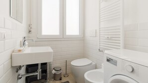 A modern bathroom with a white sink, toilet, and a washing machine. - GuestHost - Comfortable 30m2 studio flat, perfect for 2 people, located on the mezzanine floor of a building (steps to access).The accommodation is located in the Calvairate district, a residential area characterized by the green heart of Piazza Insubria (Milan)