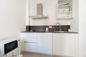 Uma cozinha moderna com armários brancos, uma coifa de aço inoxidável, uma pia embutida e um micro-ondas sobre um móvel.