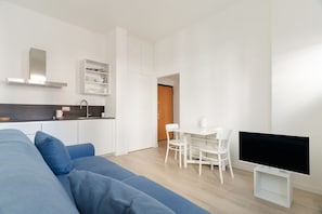 Um espaço de estar moderno e minimalista, com sofá, mesa de jantar com cadeiras, televisão e área de cozinha.