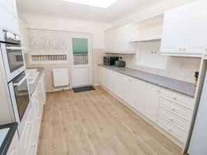 A kitchen with white cabinets, a microwave, a toaster, and a window with a green blind. - 30 Long Shepherds Drive, The Mumbles (Swansea)