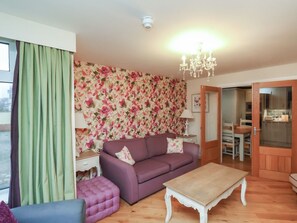 A living room with a purple sofa, a wooden coffee table, and a floral wallpaper. - Secret Garden (2 bedrooms), Bridlington (Bridlington)