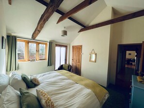 Une chambre avec un grand lit, des poutres en bois, une fenêtre et une porte.