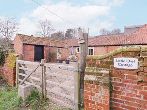 Une petite maison en briques avec une porte en bois et une pancarte indiquant « Little Owl Cottage ».
