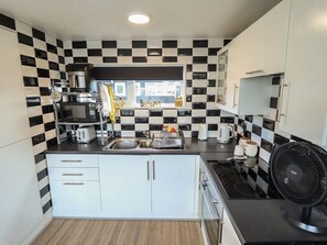 A compact kitchen with a checkered backsplash, a coffee maker, a toaster, and a fan. - 3 Cherry Blossom, Chapel St Leonards (Skegness)