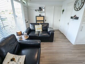 A living room with two black leather sofas, a coffee table, a wall clock, and a door with a mirror. - 3 Cherry Blossom, Chapel St Leonards (Skegness)