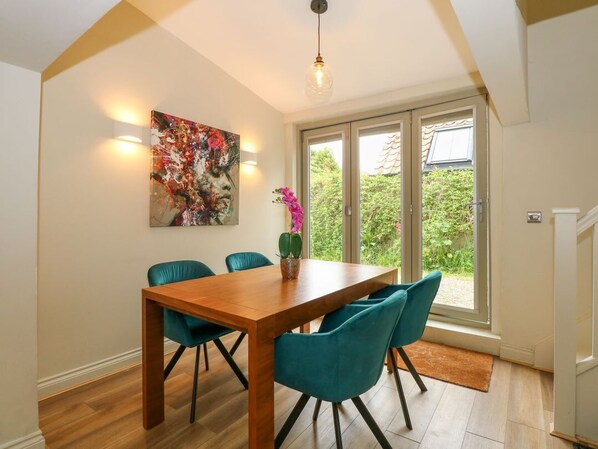 Un comedor con mesa de madera, sillas color turquesa, una planta en maceta y un amplio ventanal con vistas al verdor.