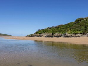 Una playa con agua cristalina, orilla de arena y una colina cubierta de hierba.
