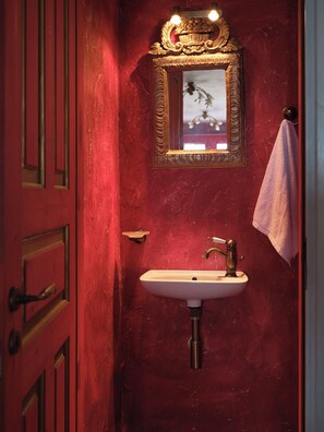 Ein rotes Badezimmer mit einem goldfarbenen Spiegelrahmen, einem weißen Waschbecken und einem Handtuch an der Wand.