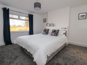 Un dormitorio con cama, cortinas, ventana y una lámpara fijada a la pared.