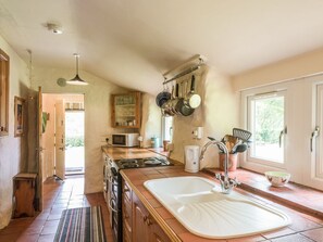 A kitchen with a large sink, hanging pots, a microwave, and a window with a view. - Hillgate House, Hemford (Shrewsbury)