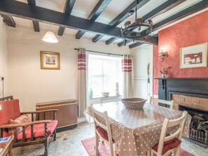 Un comedor con una mesa redonda, sillas, una araña, chimenea y ventana con cortinas.