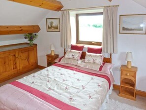Ein Schlafzimmer mit einem Bett, einem Holz-Kopfteil, Nachttischen, einem Fenster mit Vorhängen und einer Holzkommode.