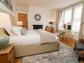 A bedroom with a bed, bedside tables, a dresser, a mirror, a fireplace, and a window with curtains. - Seafarers, Scarborough (Scarborough)