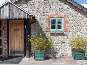 A stone building with a wooden door labeled 'Willow,' a small window, and two potted plants. - Willow, Maiden Newton (Dorchester)