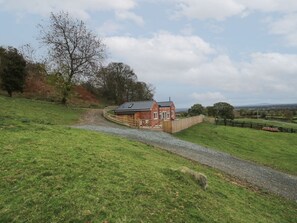 A rural house with a gravel driveway, surrounded by greenery and a fence.