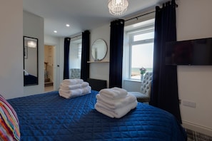 Habitación de hotel con una cama grande, televisor, candelabro y vista al mar.