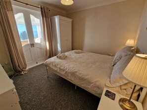 Un dormitorio con cama, mesita de noche, lámpara, armario y puerta que da a un balcón.