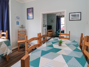 Ein Essbereich mit einem Tisch, der mit einer Tischdecke mit geometrischem Muster bedeckt ist, Holzstühlen und einer kleinen Pflanze als Mittelstück.