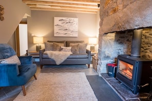 A cozy living room with a fireplace, a sofa, a chair, and a lamp. - Ynata, Trefor, Gwynedd (Caernarfon)