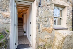A stone building with a wooden staircase leading to a door, a window, and a hanging light fixture. - Ynata, Trefor, Gwynedd (Caernarfon)
