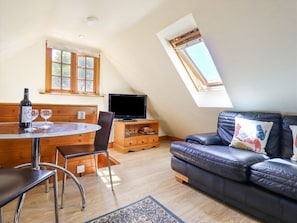Ein Loft-Zimmer mit Esstisch, Stühlen, einer Ledersofa, einem Fernseher und einem Dachfenster.