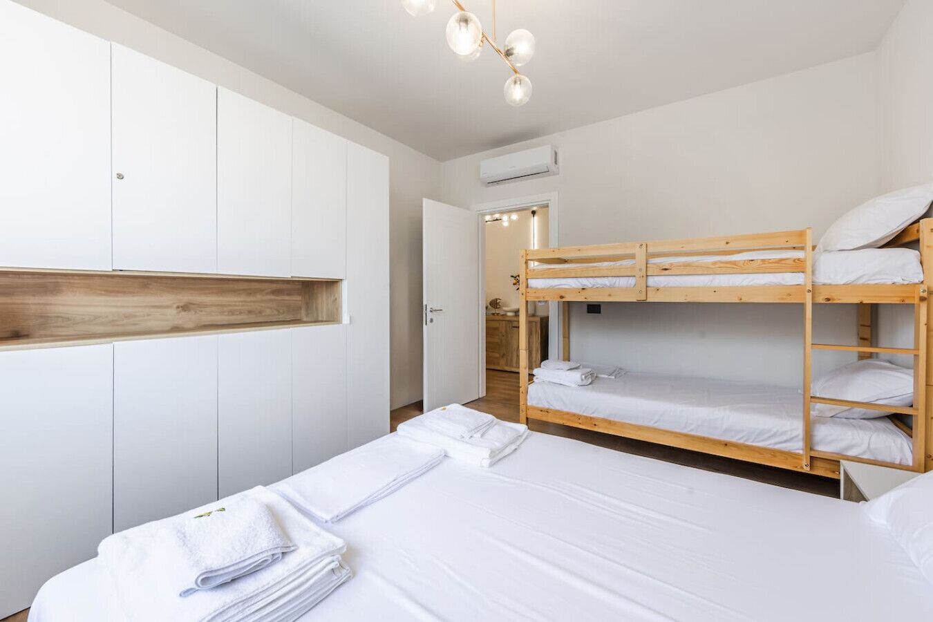 Una camera da letto con letti a castello, uno scaffale in legno, pareti bianche e un condizionatore d'aria.