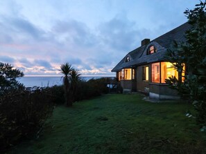 Una casa con techo inclinado, césped cuidado y vista al mar.