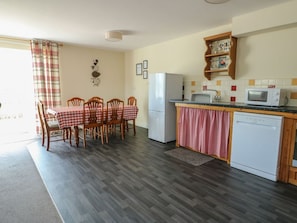 A compact kitchen with a dining area, a refrigerator, a microwave, and a sink. - Charming Ty Ni in Caeathro (Caernarfon)