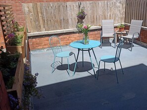 A patio with a round table, four chairs, a hanging flower basket, and a wooden fence. - Bluebell Apartment, Swanage (Swanage)