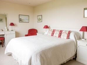 A bedroom with a large bed, a red chair, a desk with a lamp, and framed pictures on the wall. - Courtyard Cottage, Duns (Duns)