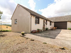 A single-story building with a sloped roof, a garage door, and a gravel driveway. - Courtyard Cottage, Duns (Duns)