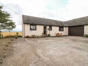 A single-story building with a concrete patio, a garage door, and a small outdoor seating area with chairs. - Courtyard Cottage, Duns (Duns)
