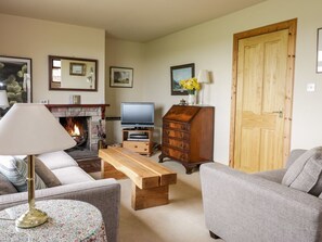 A living room with a fireplace, a television, a wooden cabinet, and a door. - Courtyard Cottage, Duns (Duns)
