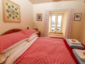 Un dormitorio con dos camas, una ventana con cortinas, un cuadro en la pared y una mesita de noche con una lámpara.