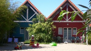 Deux maisons de plage aux façades rouge et bleue, une plage de sable et des chaises de plage.