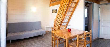 A wooden dining table with chairs, a grey sofa, a small white side table, and a wooden staircase.